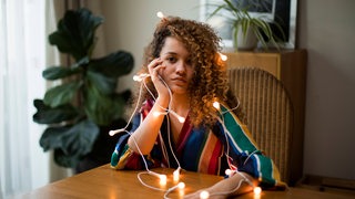 Junge Frau mit Weihnachtsbeleuchtung um den Körper schaut enttäuscht in die Kamera (Symbolbild)