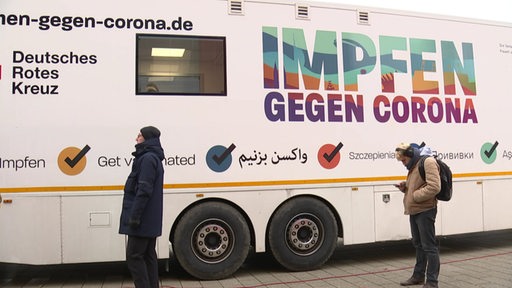 Zwei Menschen warten vor einem mobilen Corona Impfbus