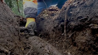 Eine Hand greift nach einem Kriegsblindgänger in einem Erdloch