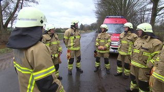 Mehrere Feuerwehrmenschen stehen neben einem Feuerwehrauto.