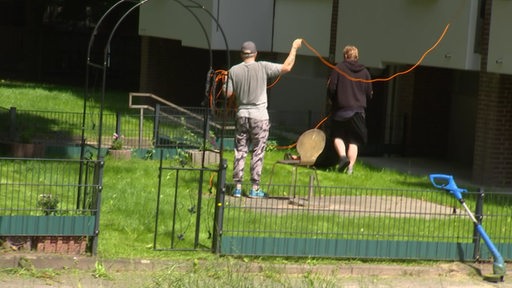 Zwei Männer mähen den Rasen vor einem Haus in Bremen-Lüssum.