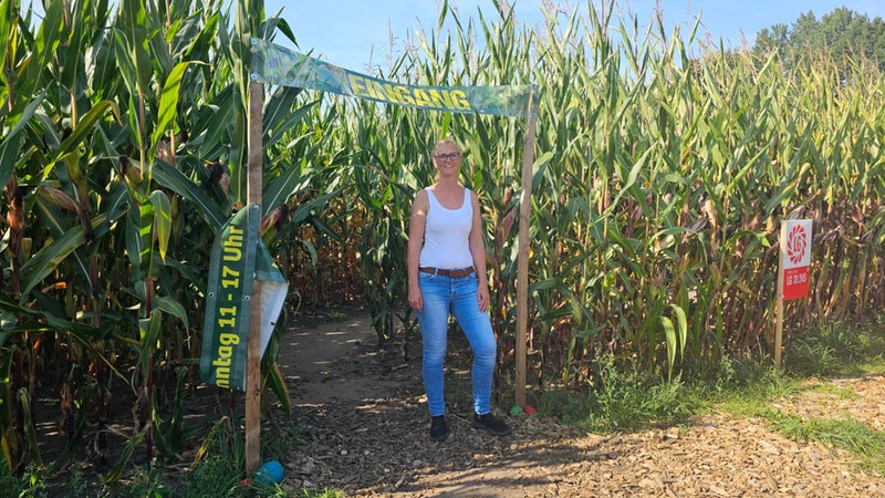 Eine Frau steht vor einem Tor in einem Maisfeld.