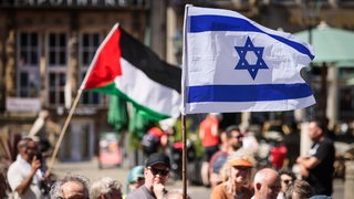 Menschen halten eine israelische und eine palästinensische Flagge auf dem Bremer Marktplatz hoch.