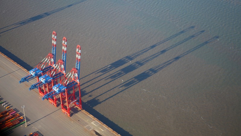 Luftaufnahme: Drei Containerbrücken am Jade-Weser-Port werfen ihren Schatten auf den Jadebusen. 