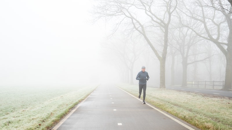 Ein Mann joggt durch eine winterliche Landschaft auf einer Straße