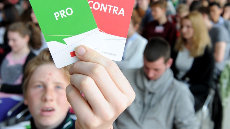 Ein Schüler hält je eine Po und Contra-Karte während einer Wahlveranstaltung der Landeszentrale für politische Bildung in Bremen in die Höhe.