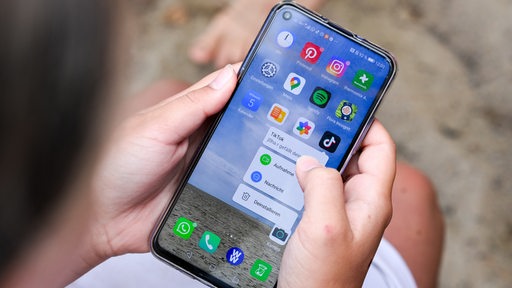 Eine Jugendliche hält ein Smartphone in den Händen, auf dem u.a. die TikTok-App zu sehen ist.