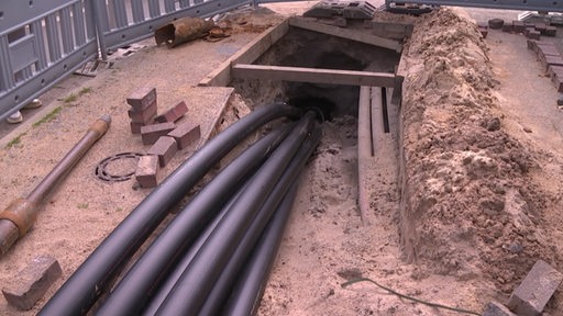 Mehrere Stromkabel gehen auf einer Baustelle in den Boden.