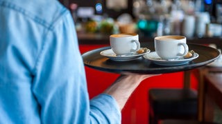 Ein Ober trägt ein Tablett mit zwei Cappuccini