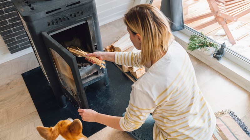 Eine Frau legt Holz in ihren Kamin im Wohnzimmer.