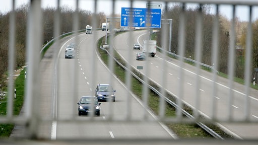 Blick durch das Gitter einer Brücke auf eine Autobahn.