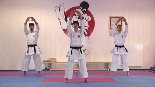 Drei Männer in traditionellen Karate Uniformen stehen in einem Dojo