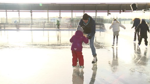 Ein Vater hilft seinem Kind beim Eislaufen.