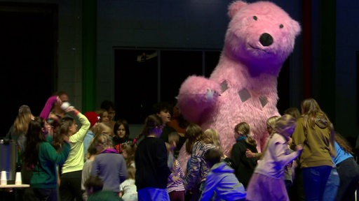 Kinder bewerfen einen rosa Bären mit weißen Bällen 