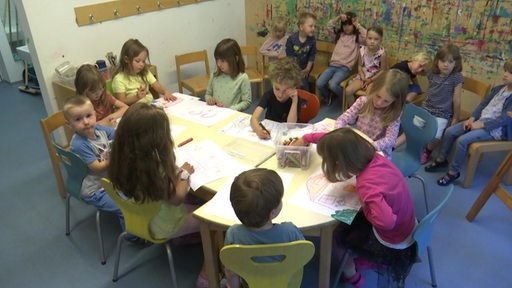 Kinder sitzen am Tisch und malen.