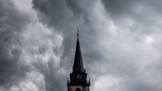 Dunkle Wolken eines Schauers sind am Abend am Himmel über einem Kirchturm zu sehen.