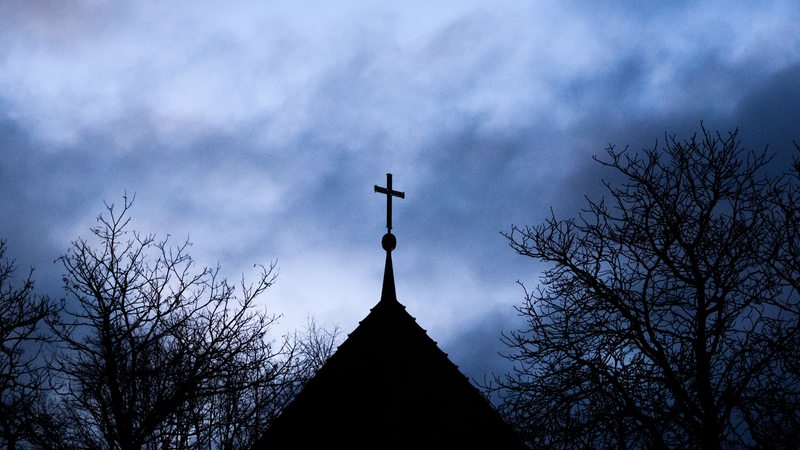 Dunkle Wolken ziehen über das Kreuz auf einer evangelischen Kirche in der Region Hannover hinweg. 