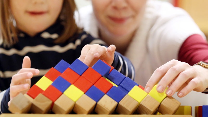 Eine Erzieherin spielt gemeinsam mit einem Kindergartenkind mit Holzspielzeug.