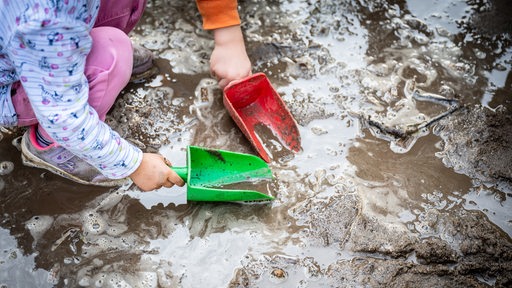 Kinder spielen mit Schaufeln in Sand und Matsch