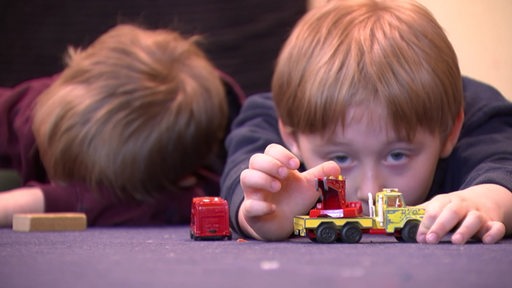 Zwei Kinder die mit einer Spielzeugfeuerwehr spielen.