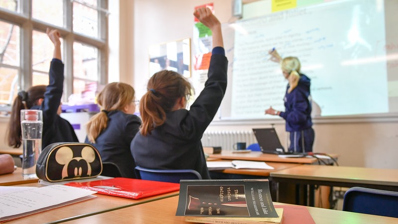 Schülerinnen in Schuluniform sitzen in einem Klassenzimmer und melden sich.