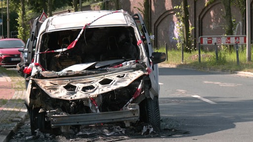 Zu sehen ist ein ausgebranntes Auto am Straßenrand.