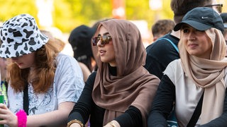 Drei Frauen sind auf einem Konzert, zwei von ihnen tragen ein Kopftuch.