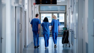 Krankenhauspersonal, von hinten gesehen, geht über einen Klinikflur (Symbolbild)