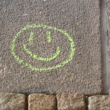 Auf Steinen wurden mit Kreide zwei Smileys gemalt. Einer guckt glücklich und ist grün und einer guckt unglücklich und ist rot.