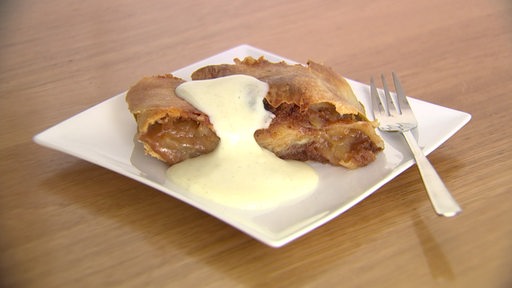 Auf einem Teller liegt ein Stück Apfelstrudel mit Vanillesauce übergossen.