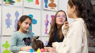 Drei Mädchen in einem Bastelraum rings um eine Hasen-Figur aus Bronze