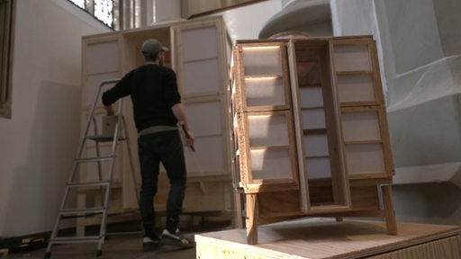 Eine Person steht vor einem Holzkonstrukt in einer Kirche.