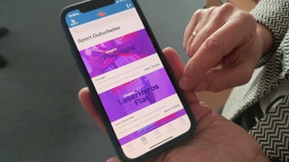 Zwei Hände halten ein Smartphone, auf dem "Sport Gutschein" zu lesen ist.
