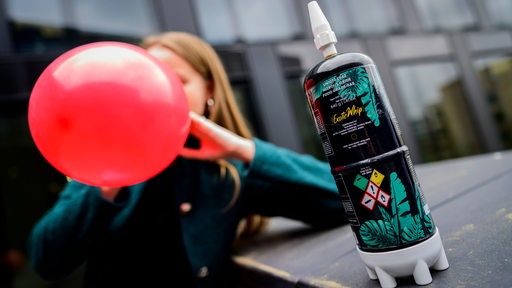 Eine Frau zieht an einem Luftballon. Im Vordergrund steht eine Lachgas-Flasche.