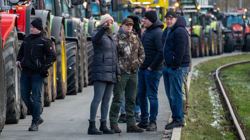 Menschen stehen vor einer Kolonne von Traktoren auf einer Straße.