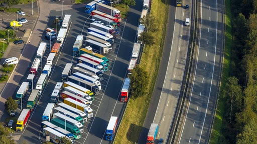 Eine Luftaufnahme zeigt eine Autobahnraststätte von oben, auf der viele Lkw stehen.