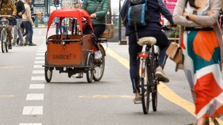 Fahrradfahrer und Lastenradfahrer fahren auf einem Fahrradstreifen auf der Fahrbahn.