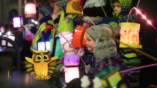 Kinder laufen mit leuchtenden Laternen bei einem Umzug mit.