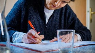 Ein Mann sitzt an einem Tisch und streicht mit einem roten Stift etwas an.