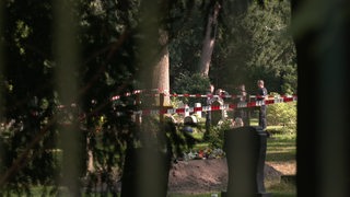 Polizeibeamte stehen hinter einer Absperrung auf dem Friedhof.