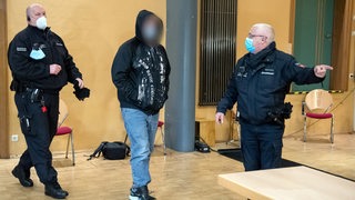 Ein Mann in Jeans und Kapuzenjacke folgt der Anweisung eines Justizbeamten.