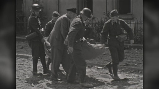 Militärs tragen gemeinsam eine Barge auf der sich vermutlich eine verwundete oder tote Person befindet.