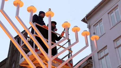 Zwei Personen entzünden Flamme bei Lichterfest Chanukka.