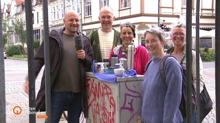 Wettermoderator Heyko Habben und einige Menschen stehen auf dem Delmemarkt um einen Stromkasten herum.