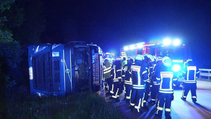 Lkw liegt umgekippt auf der A1, Feuerwehrkräfte stehen daneben