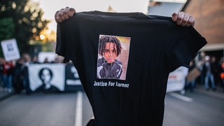Ein Demonstrant hält vor einer Kundgebung ein schwarzez T-Shirt in die Kamera, auf dem der von Polizeischüssen getötete Lorenz aus Oldenburg abgebildet ist.