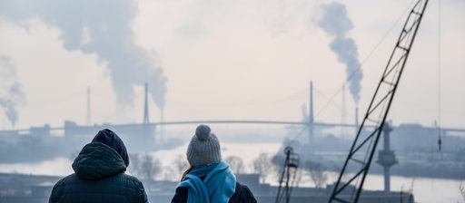 Passanten betrachten bei kühlem Wetter die Köhlbrandbrücke und die umliegenden Industrieanlagen im Hamburger Hafen.