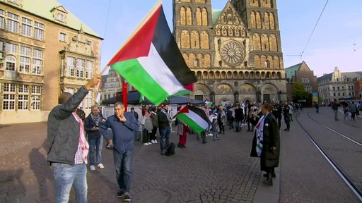 Mehrere Menschen stehen vor dem Bremer Dom und schwenken Palästina-Flaggen.