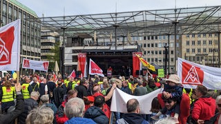 Menschen stehen vor einer Bühne und schwenken Verdi- und IGM-Flaggen.