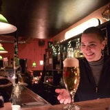 Junge kurzhaarige Frau hinter einer Theke präsentiert ein Bier